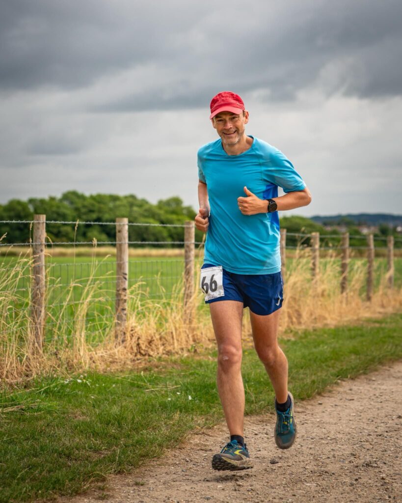 A man in a blue top running on a gravel path in the countryside.