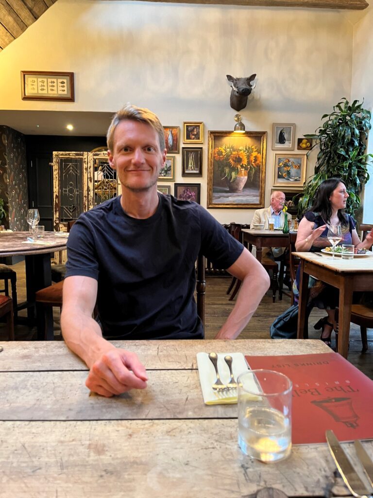 A man sitting down in a pub, waiting for his food and smiling,